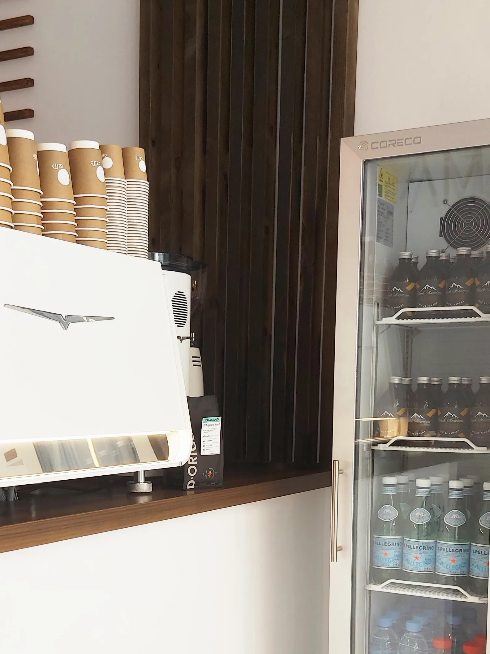 Cafetera Victoria Arduino blanca en la barra, con vasos de cartón apilados encima