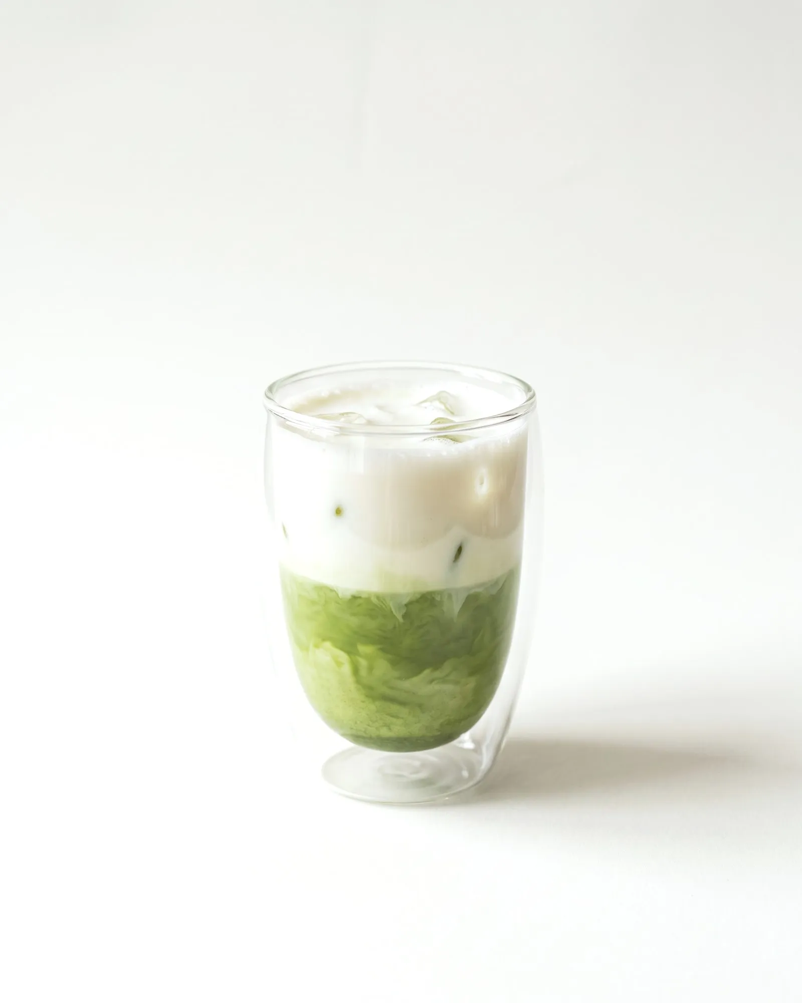 Iced matcha latte en vaso de vidrio doble: leche arriba, matcha abajo y hielo